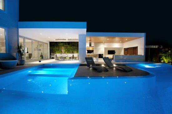 Residential swimming pool illuminated with blue Spa Electrics underwater pool lighting at night